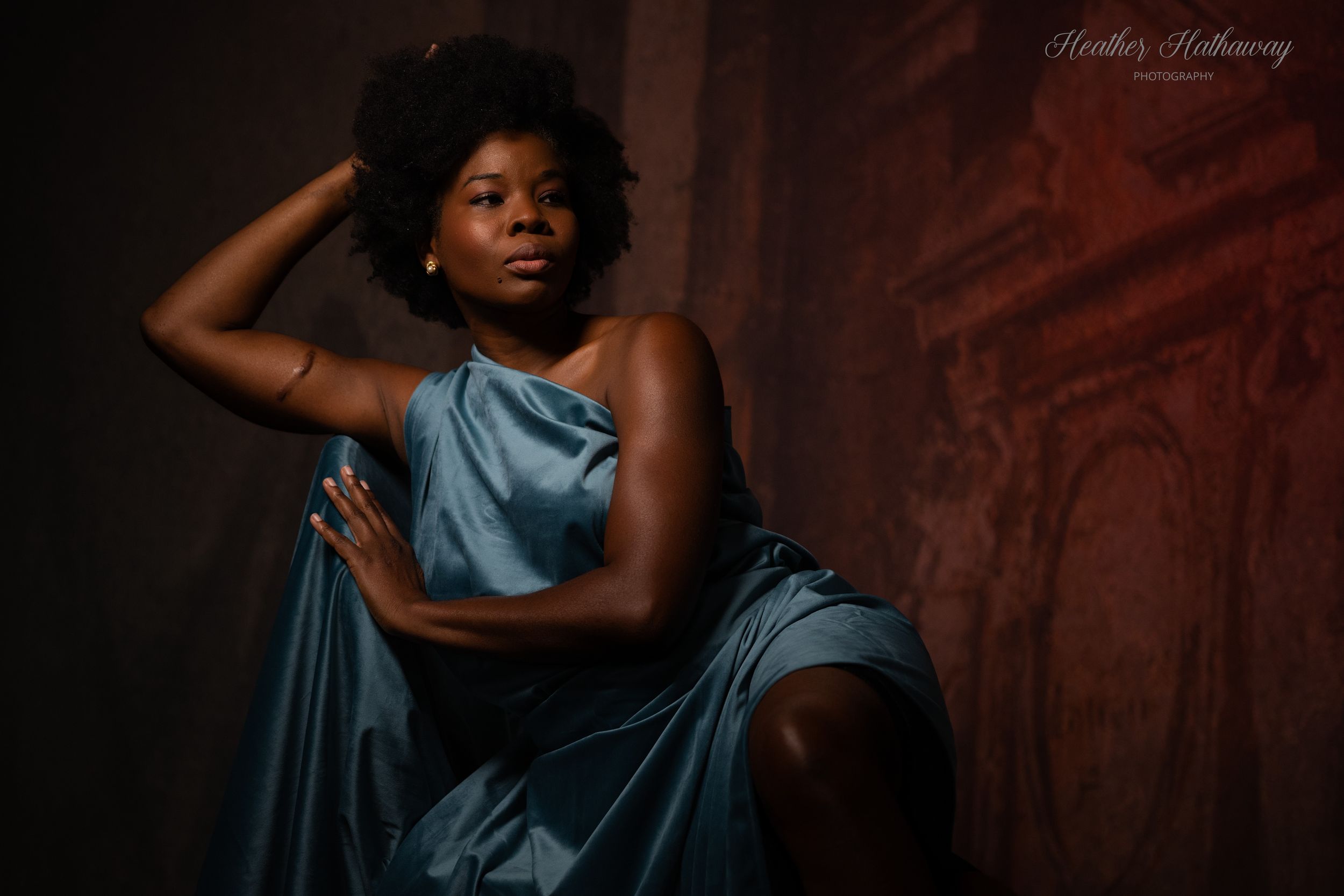 A stylish blue satin dress flows elegantly against a dark rustic backdrop in this artistic portrait.