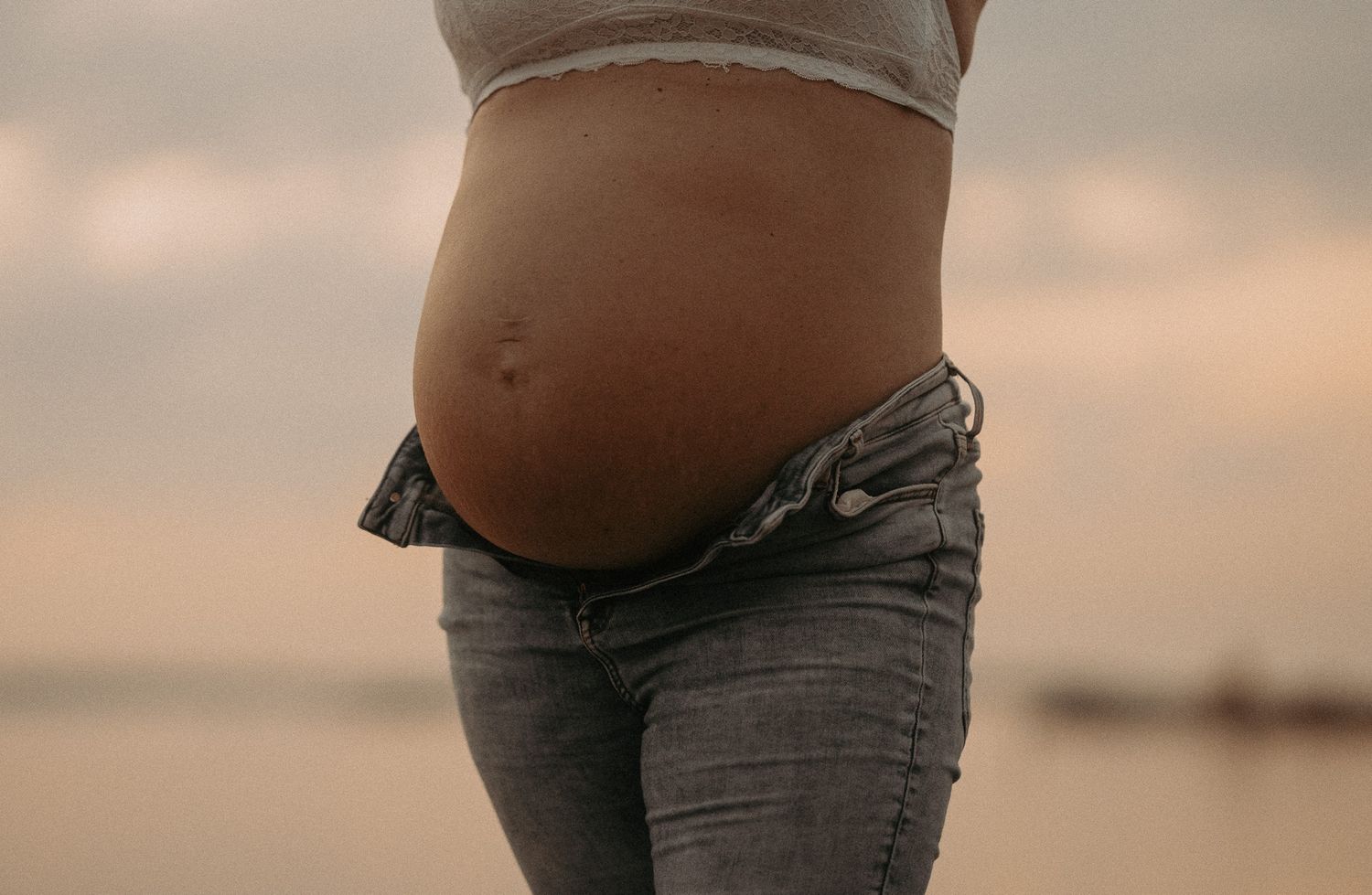 Close-up silhouette of a pregnant belly against a sunset sky.