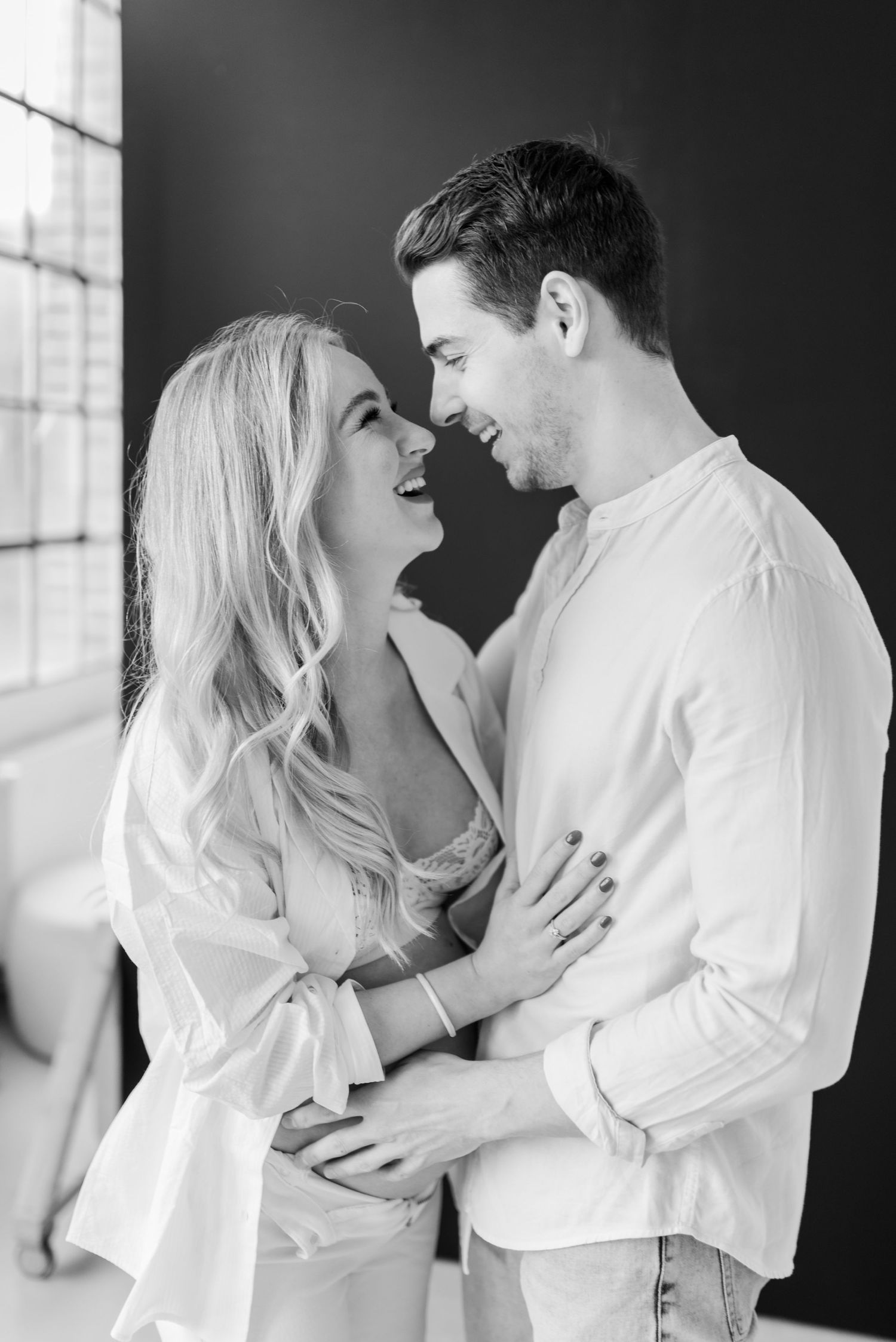 Romantic black and white photography series showing an intimate couple embracing in white clothing against dark background.