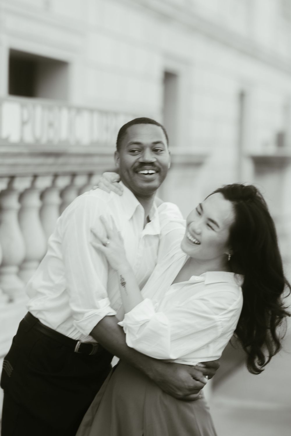 A joyful couple embraces and laughs together against a stone building backdrop.