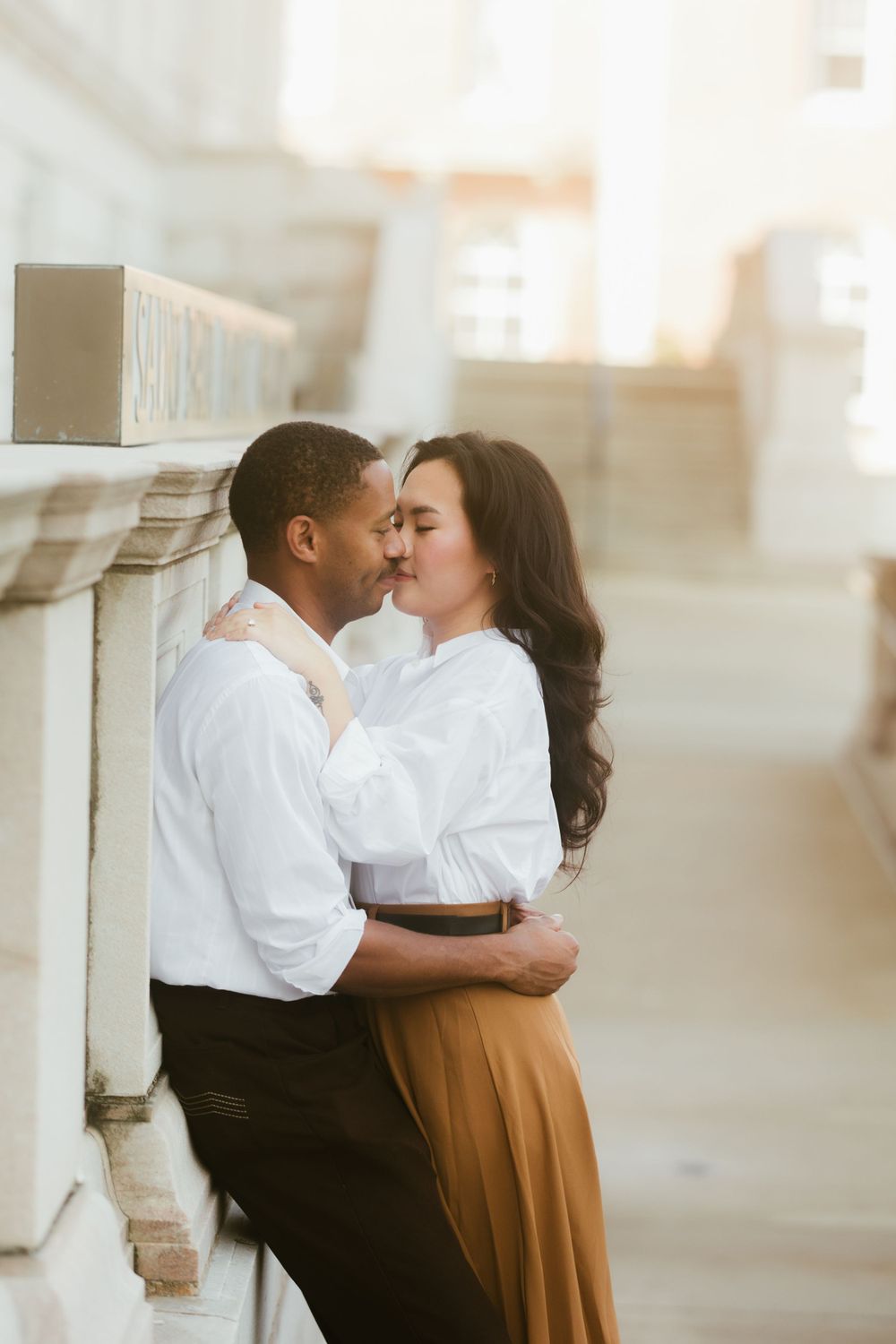 A tender moment shared between two people against a sunlit stone wall.