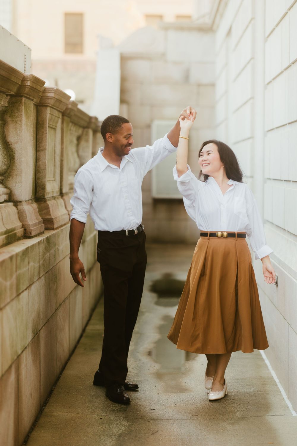 A couple dances playfully in a stone corridor with natural lighting.