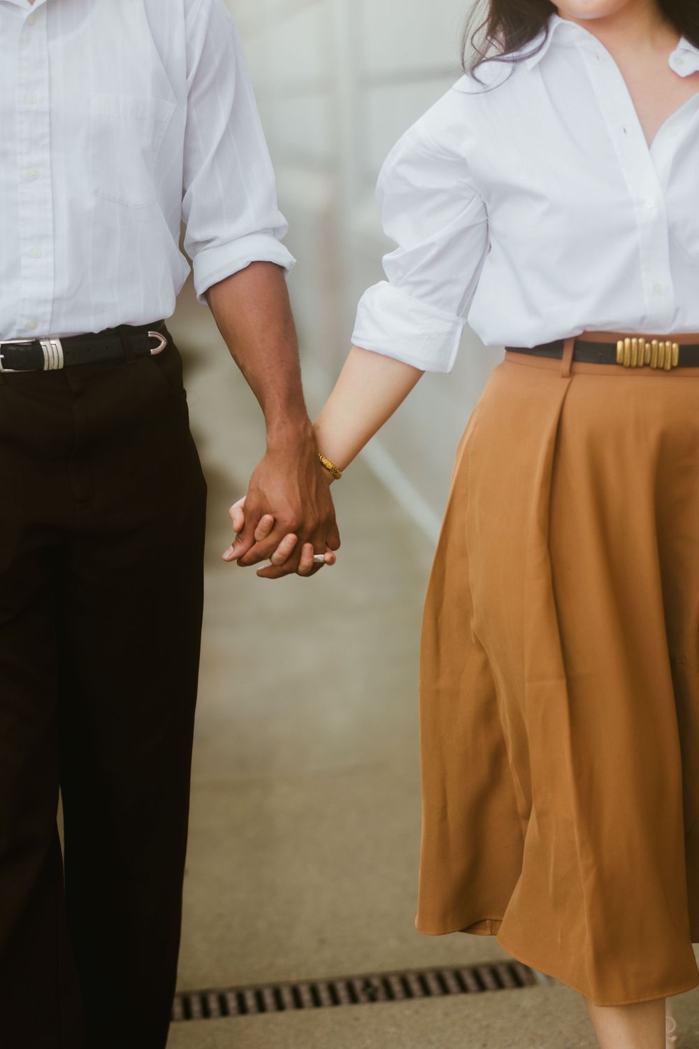 Close-up of couple holding hands wearing contrasting white shirts and brown and black bottoms.
