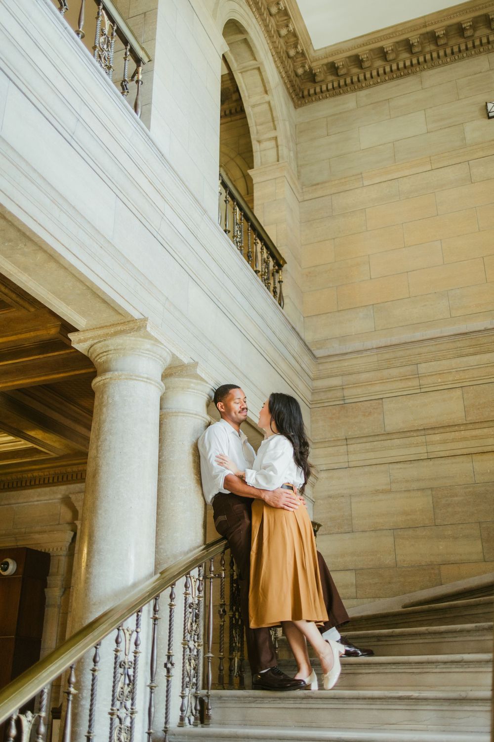 Romantic couple standing close together on grand marble staircase inside historic building.