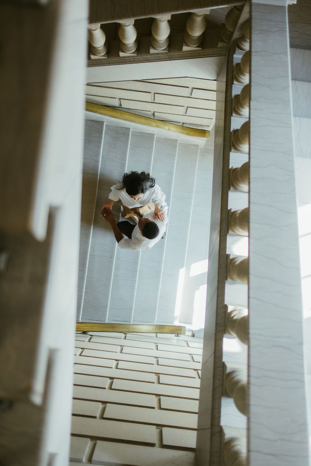Bird's eye view of couple embracing on white tiled floor with architectural details.