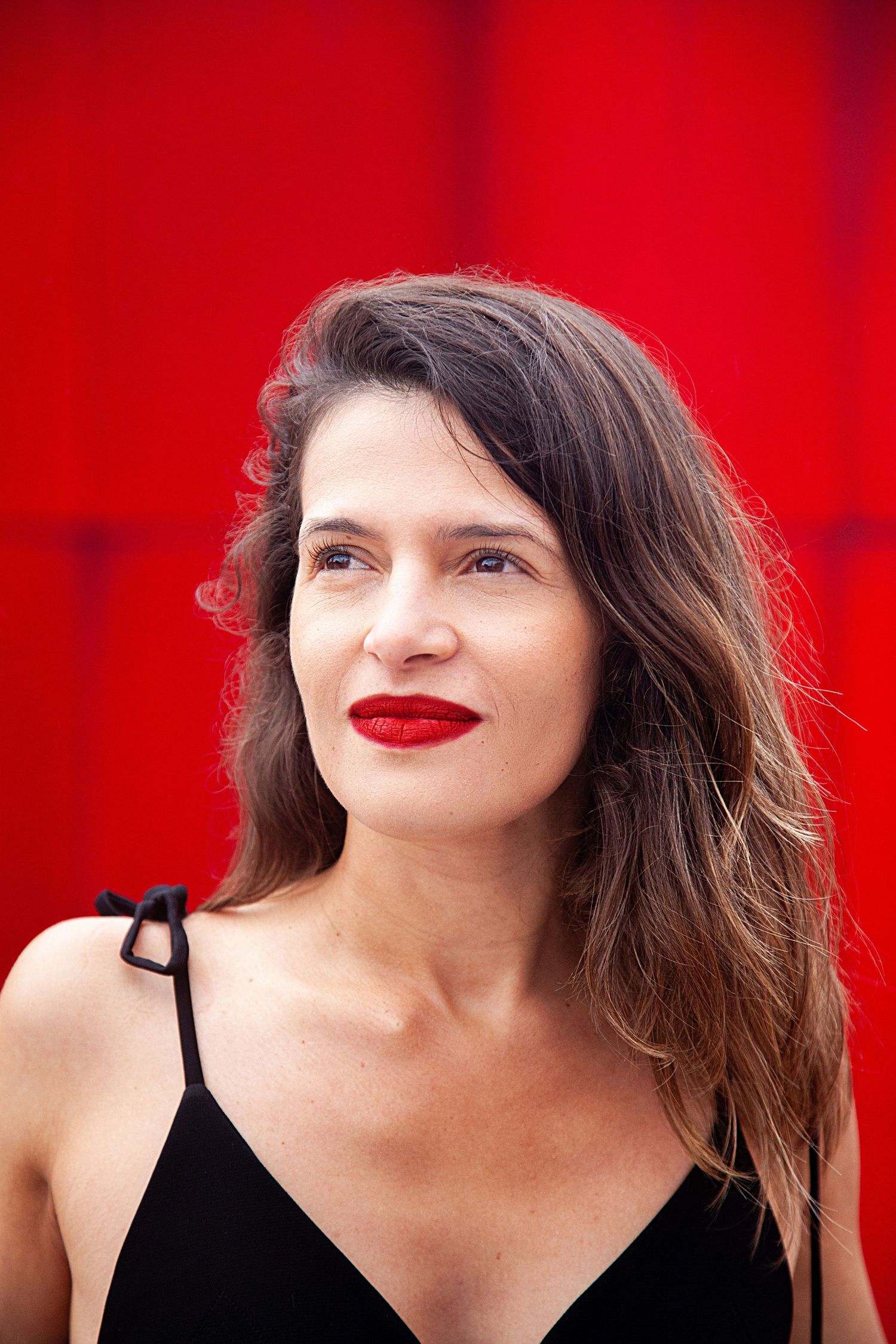 Portrait against vibrant red background with bold red lipstick and black top.