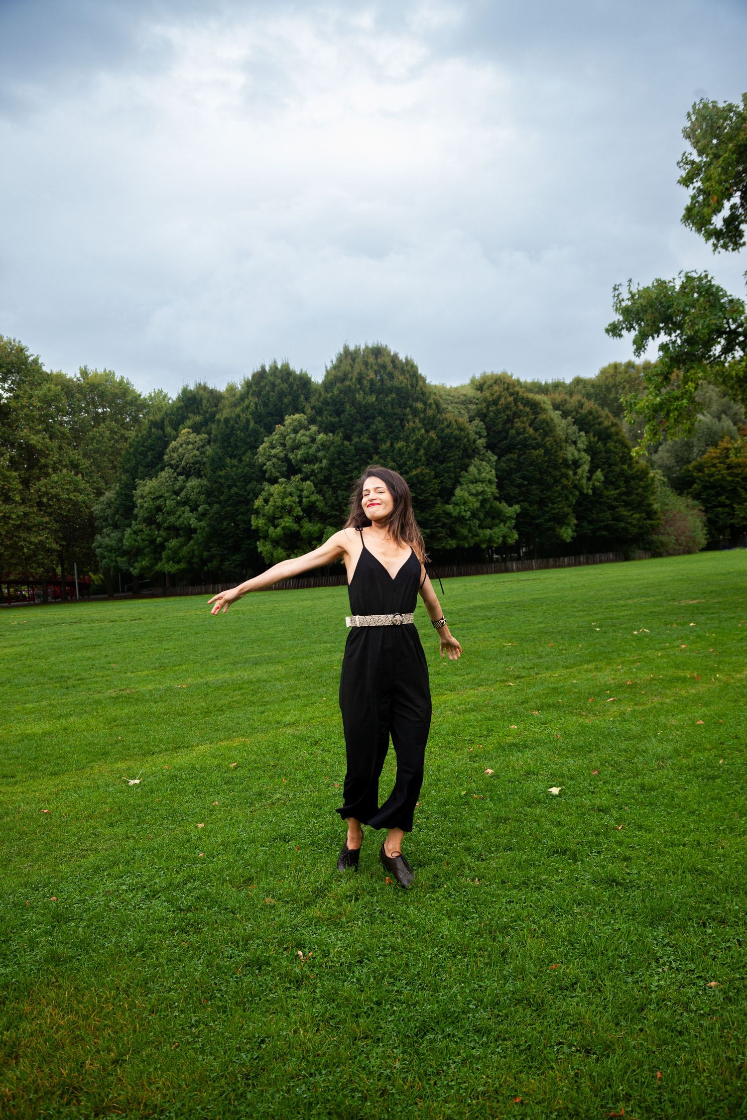 A person in black clothing jumps with outstretched arms on a grassy hill.