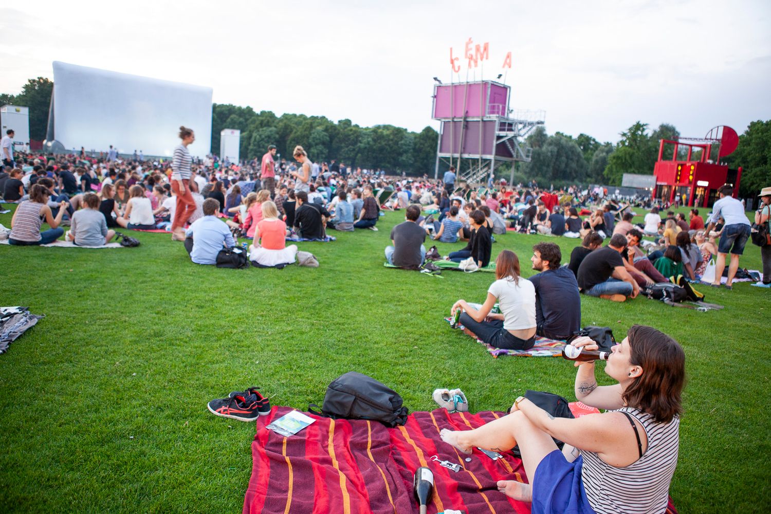 People relaxing on blankets at outdoor cinema event in park during sunset.