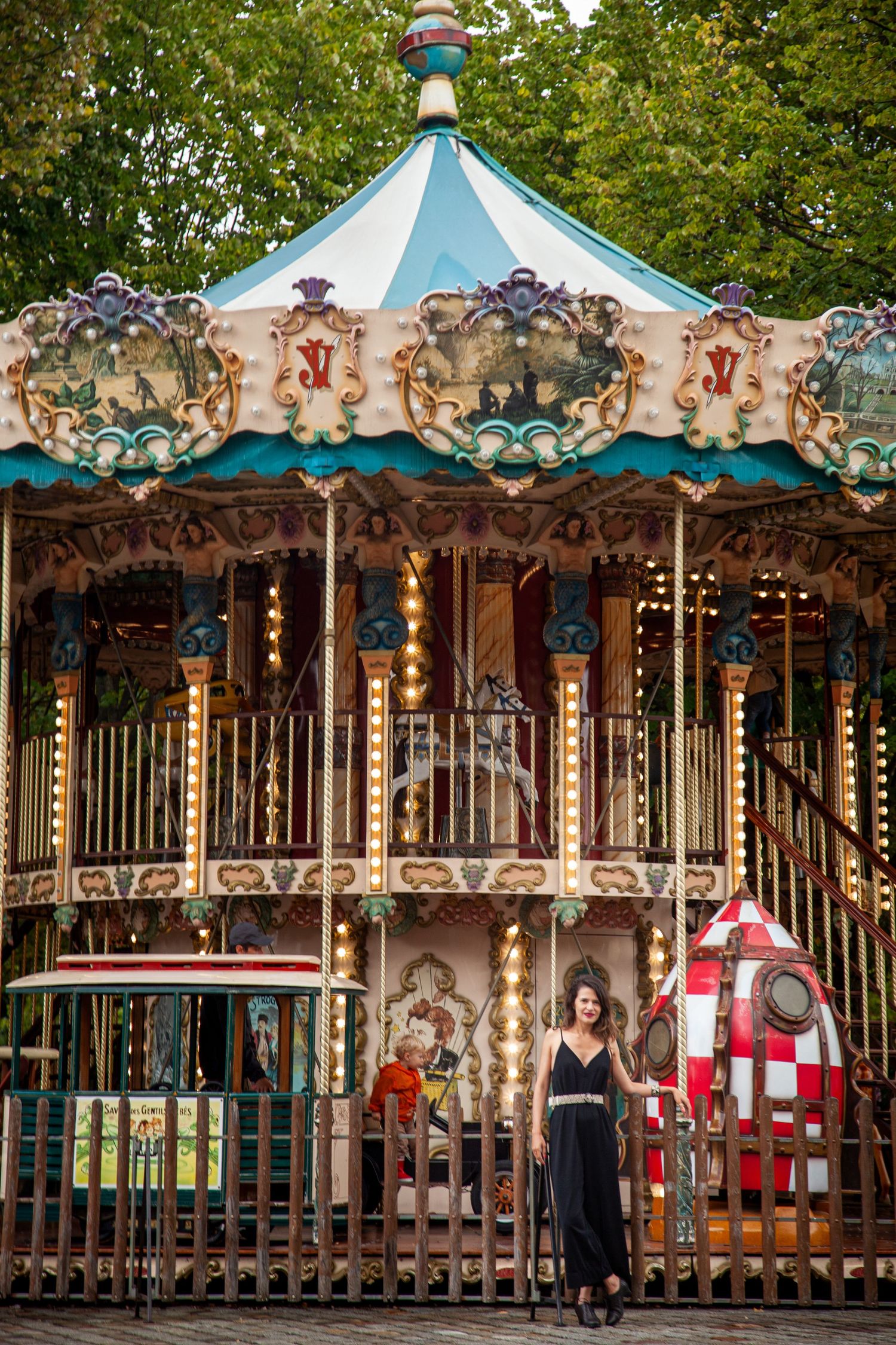 Vintage carousel with ornate turquoise and gold decorations in a park setting.