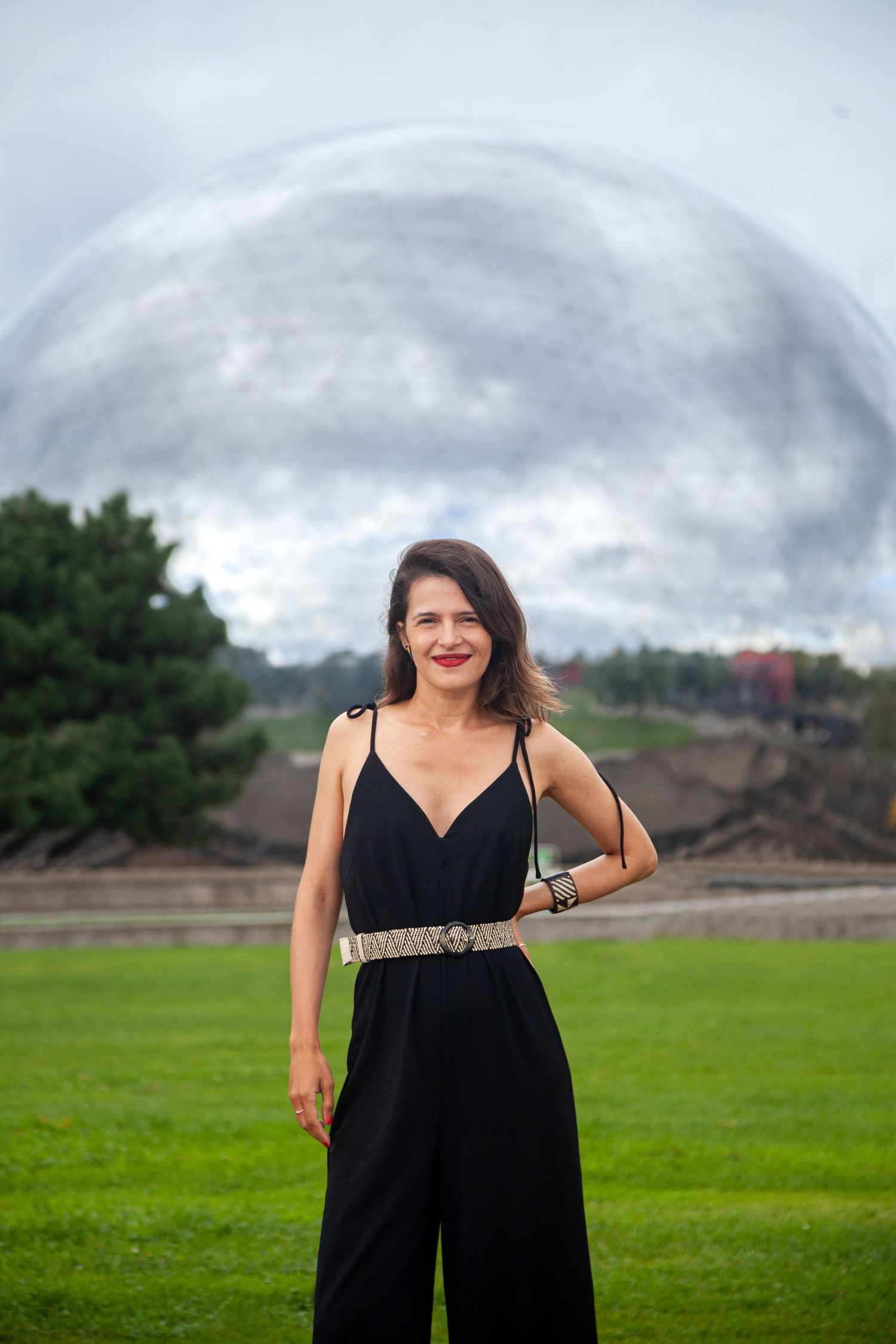 Outdoor portrait with dramatic cloudy sky and geodesic dome structure in background.