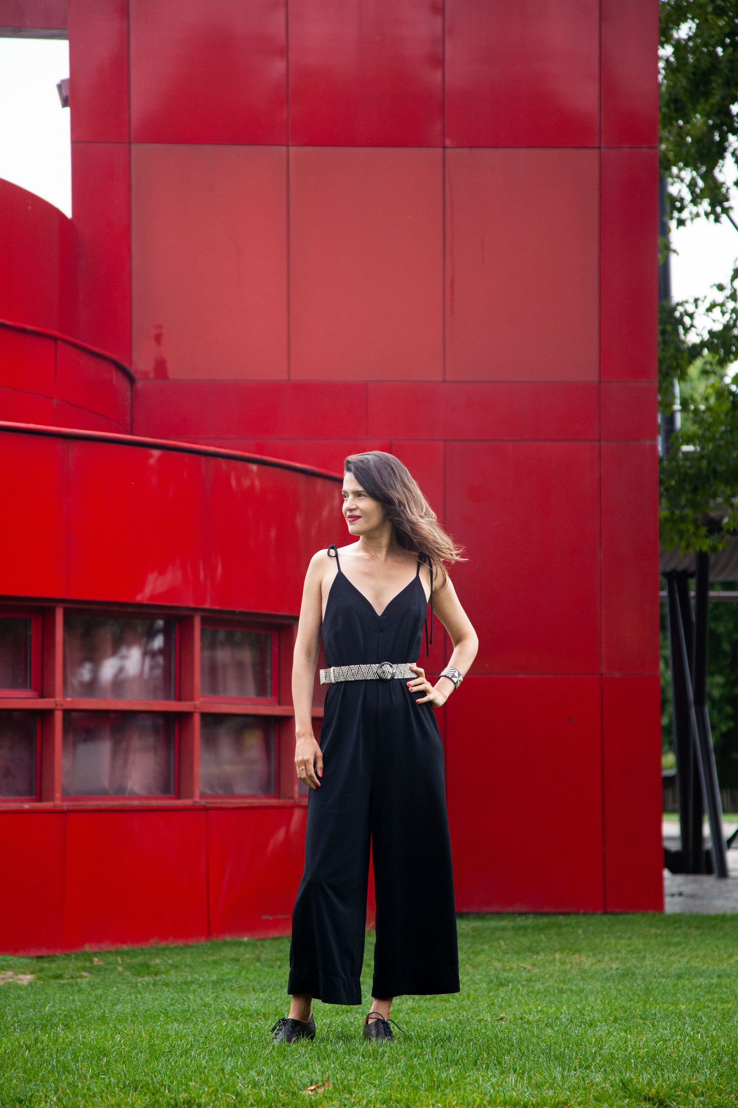 Fashion photo featuring black jumpsuit against modern red architectural backdrop.