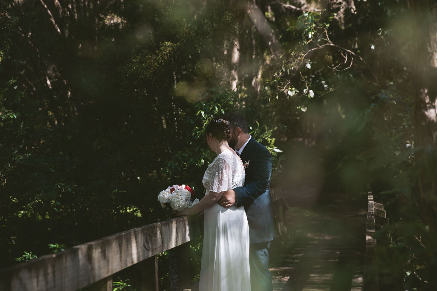 Couple shares private moment on rustic bridge surrounded by forest foliage.