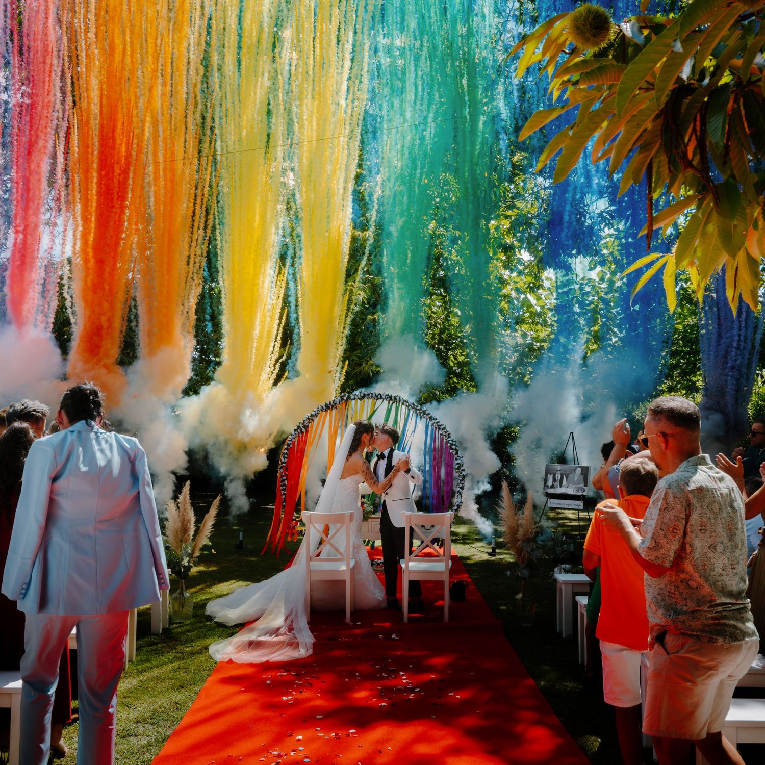 Colorful smoke bombs create rainbow effect at outdoor wedding celebration.
