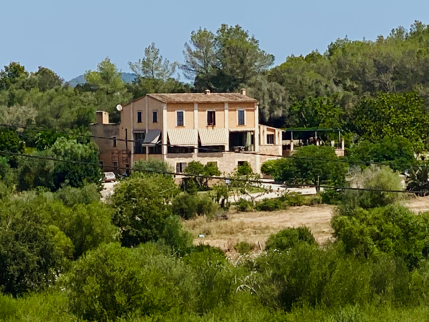 Mediterranean villa with stone facade nestled among green trees and shrubs on a sunny hillside in Mallorca.