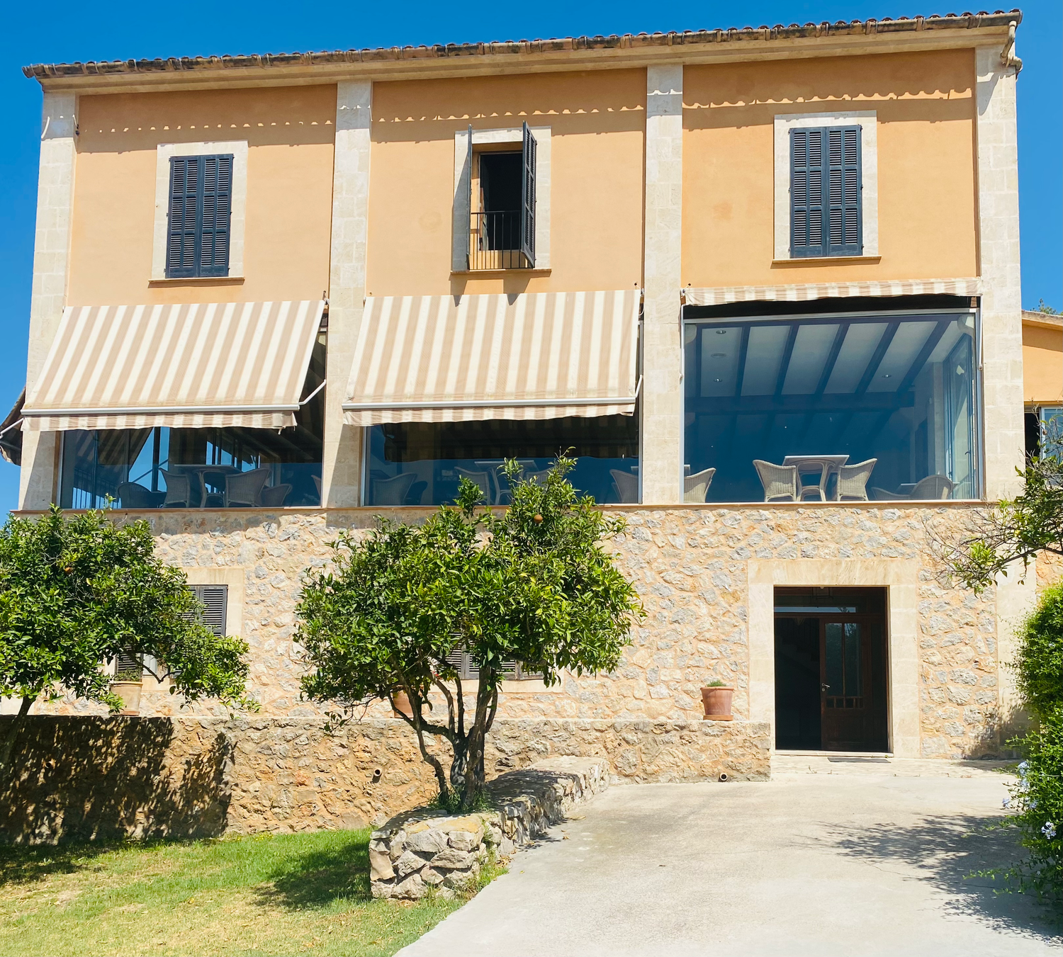 Stone villa exterior with beige walls and multiple windows overlooking a Mediterranean landscape on a sunny day.