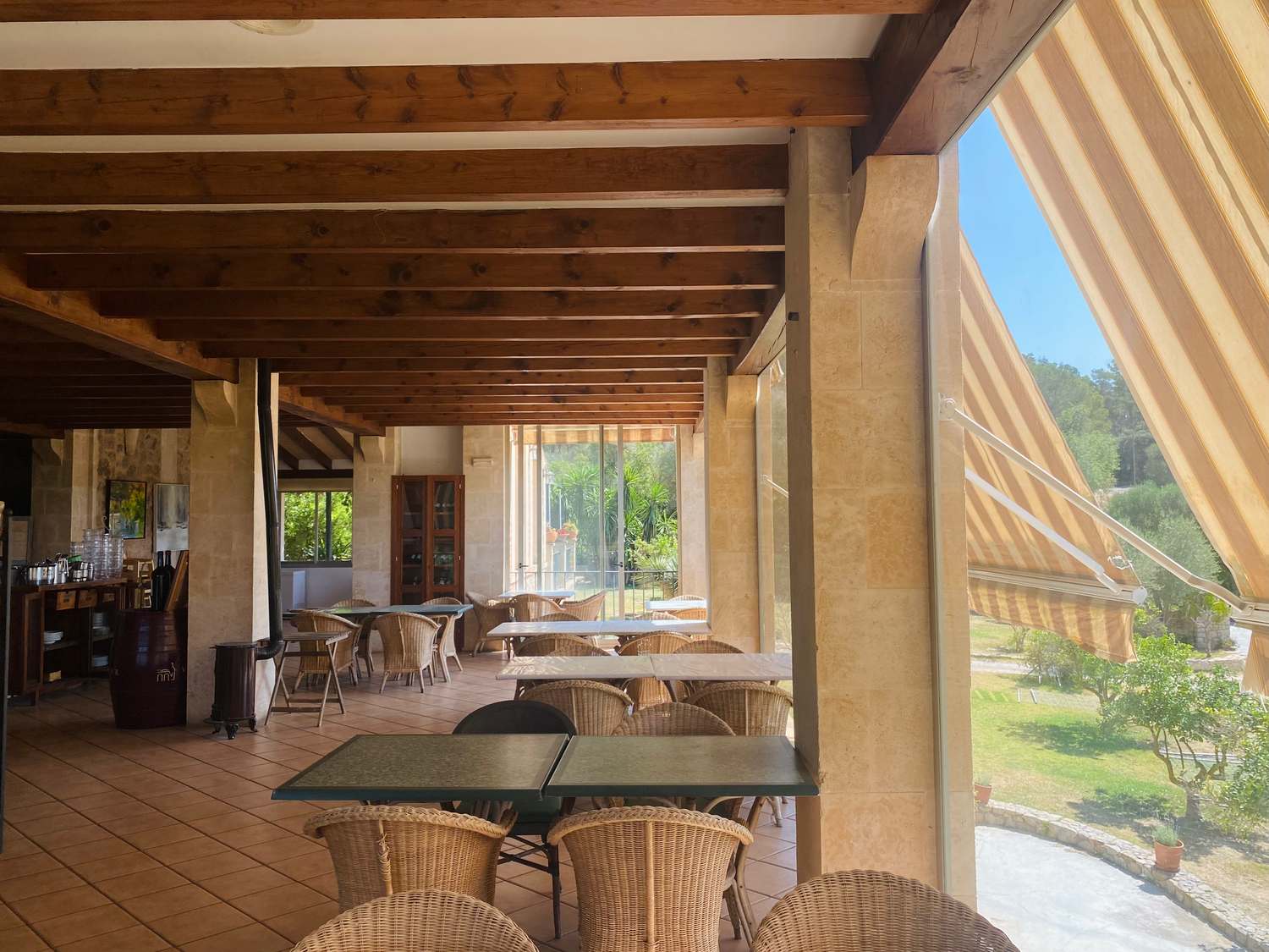 Covered outdoor dining terrace with wicker chairs and wooden beams overlooking a scenic countryside view.