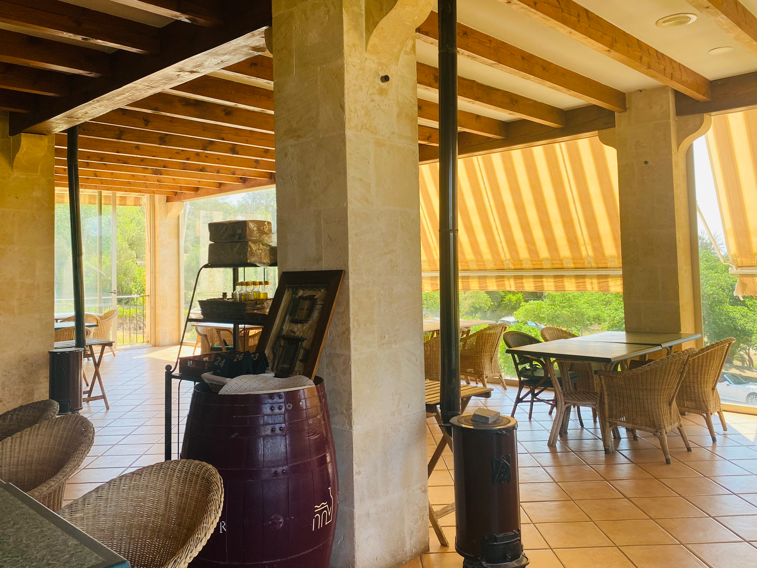 A covered outdoor patio with wicker chairs, wooden beams, and striped awning features a vintage wine barrel and arcade machine.