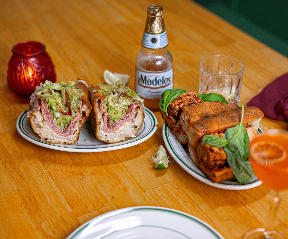 Bar food spread on wooden table with sandwiches, chicken wings, beer and table settings.