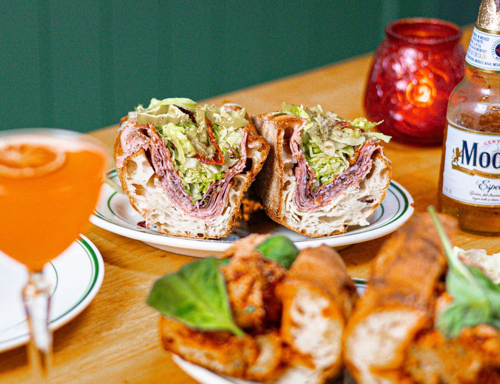 Deli sandwiches on a plate with shredded lettuce and a beer bottle garnished with fresh basil leaves.
