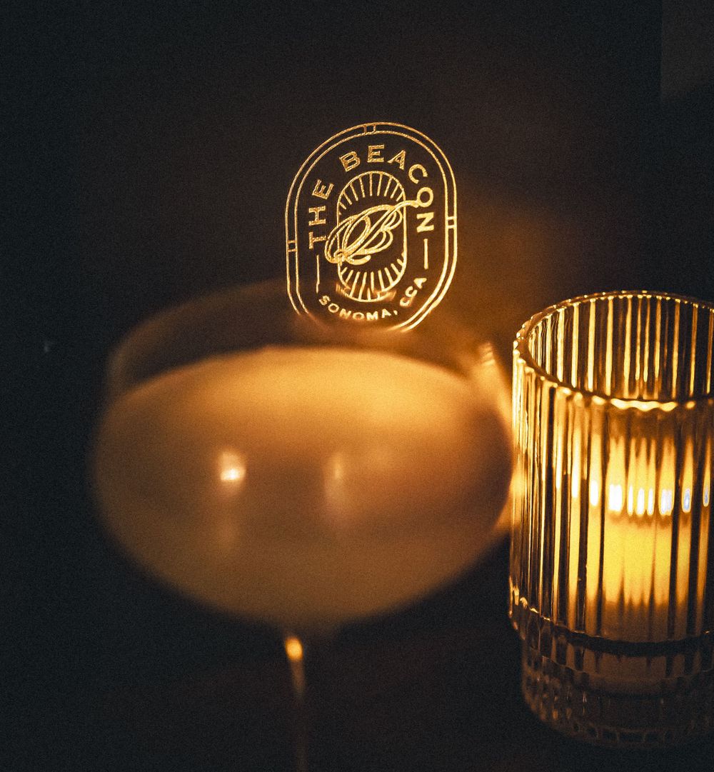 Illuminated gold logo and glassware casting warm shadows in dark setting.