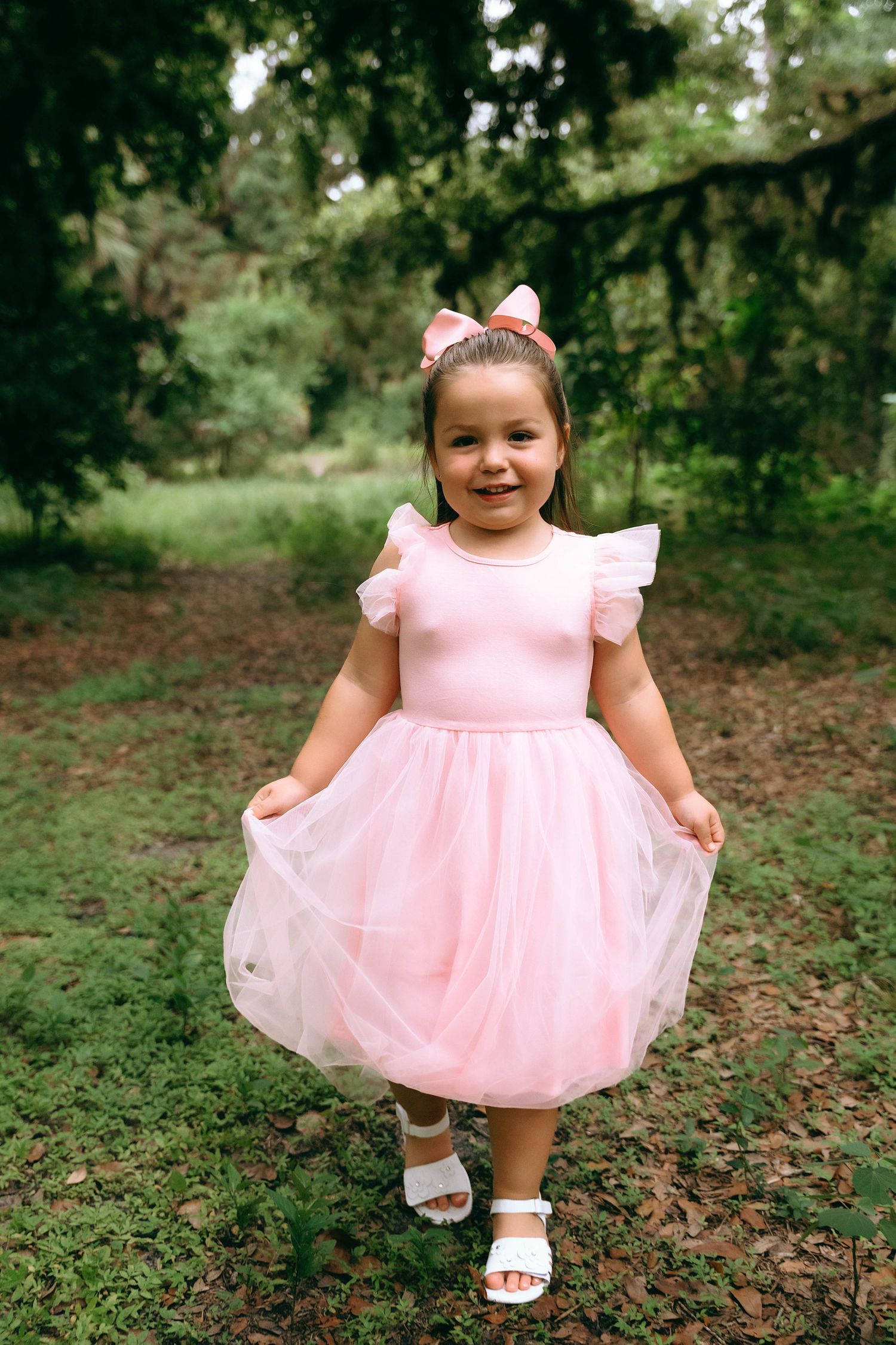 Sweet pink princess dress with ruffled sleeves and tulle skirt shown in an outdoor woodland setting.