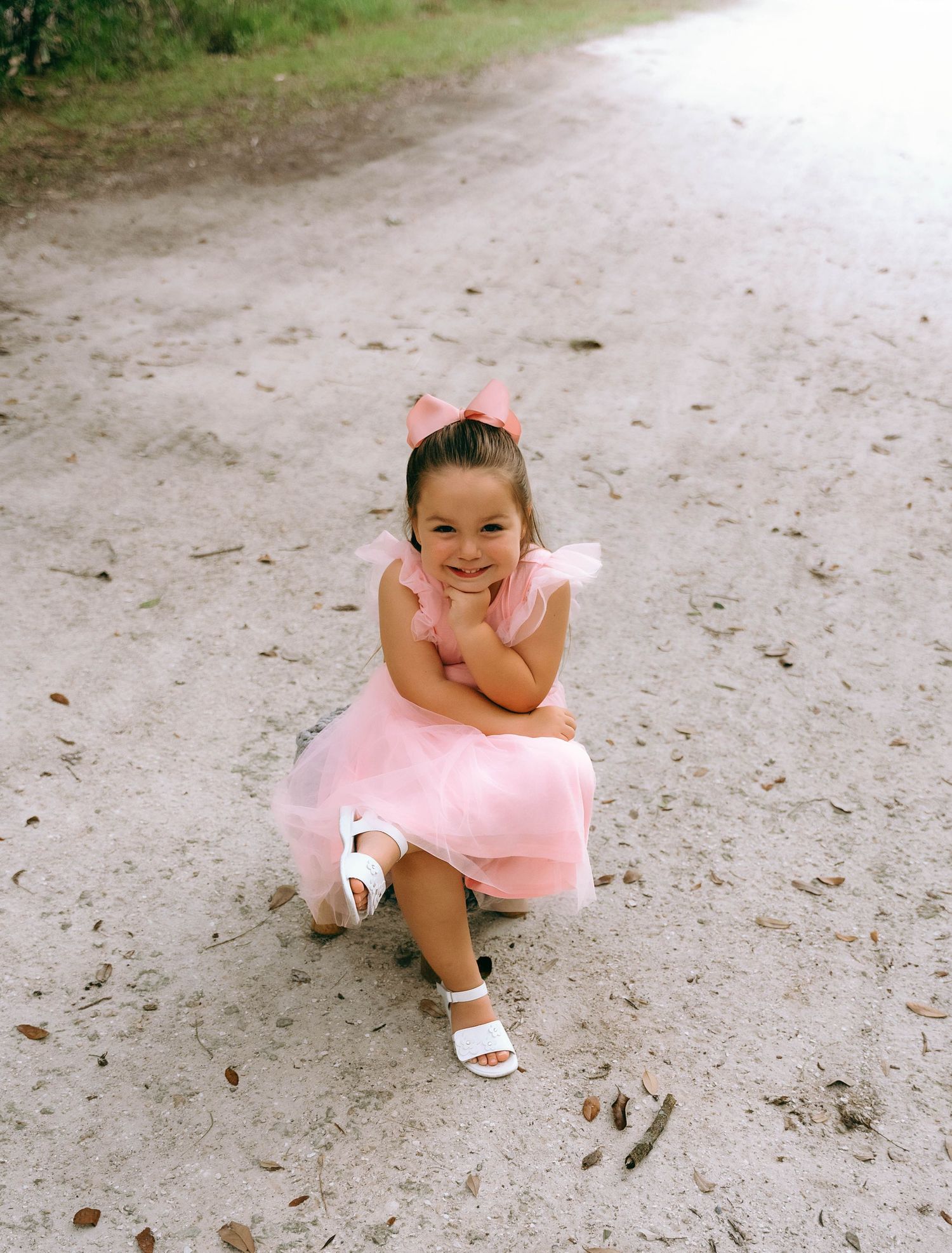 A sequence of five similar photos showing a young dancer in a pink tutu sitting on a sandy ground.