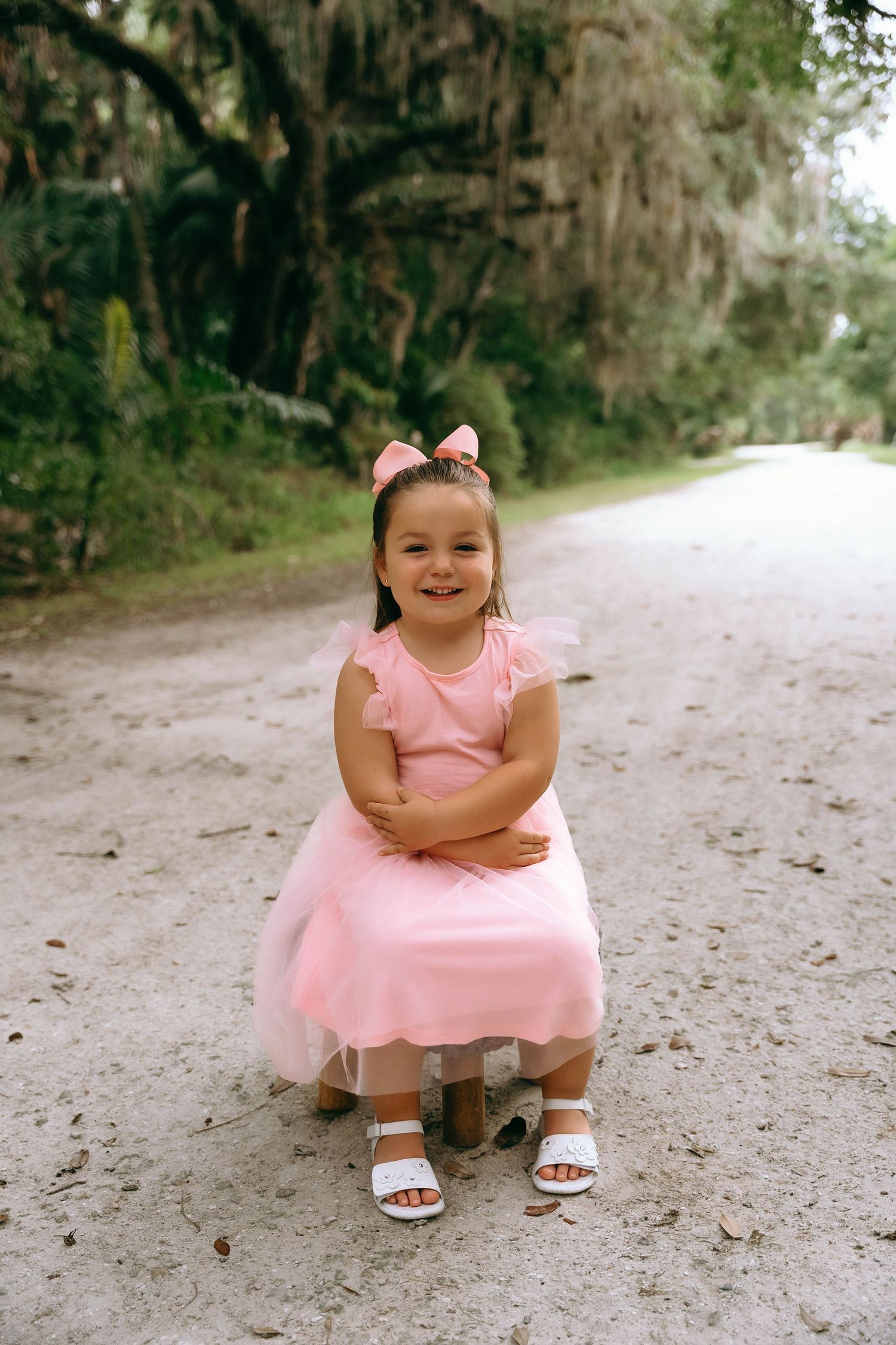 A person in a pink dress sits crouched on a dirt path surrounded by trees in different poses.