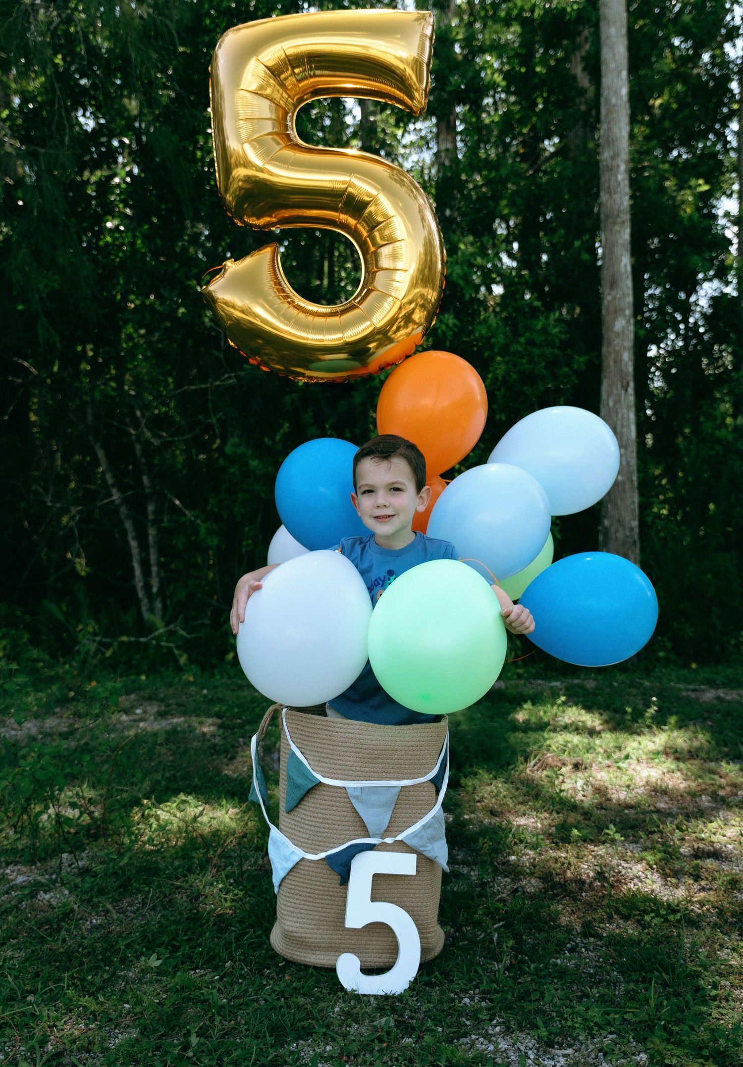 A birthday celebration setup with a large gold number 5 balloon and colorful party balloons arranged outdoors.
