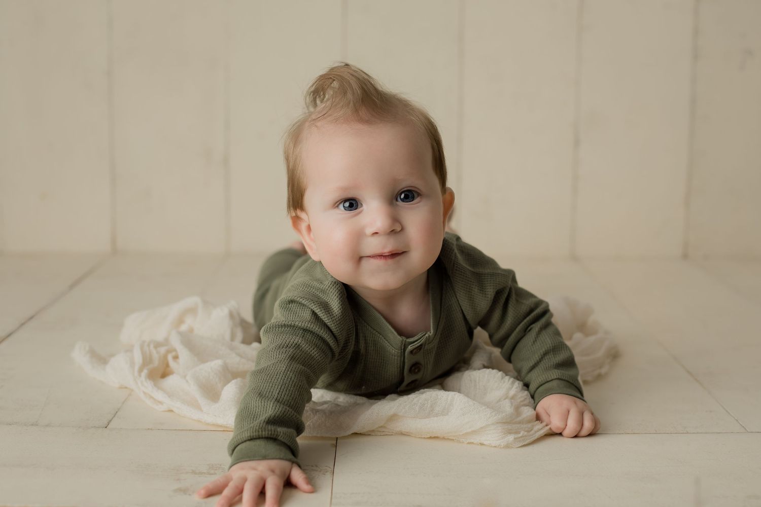 Photo of a six month baby boy wearing green laying on his tummy and smiling at the camera for his studio milestone portrait session.