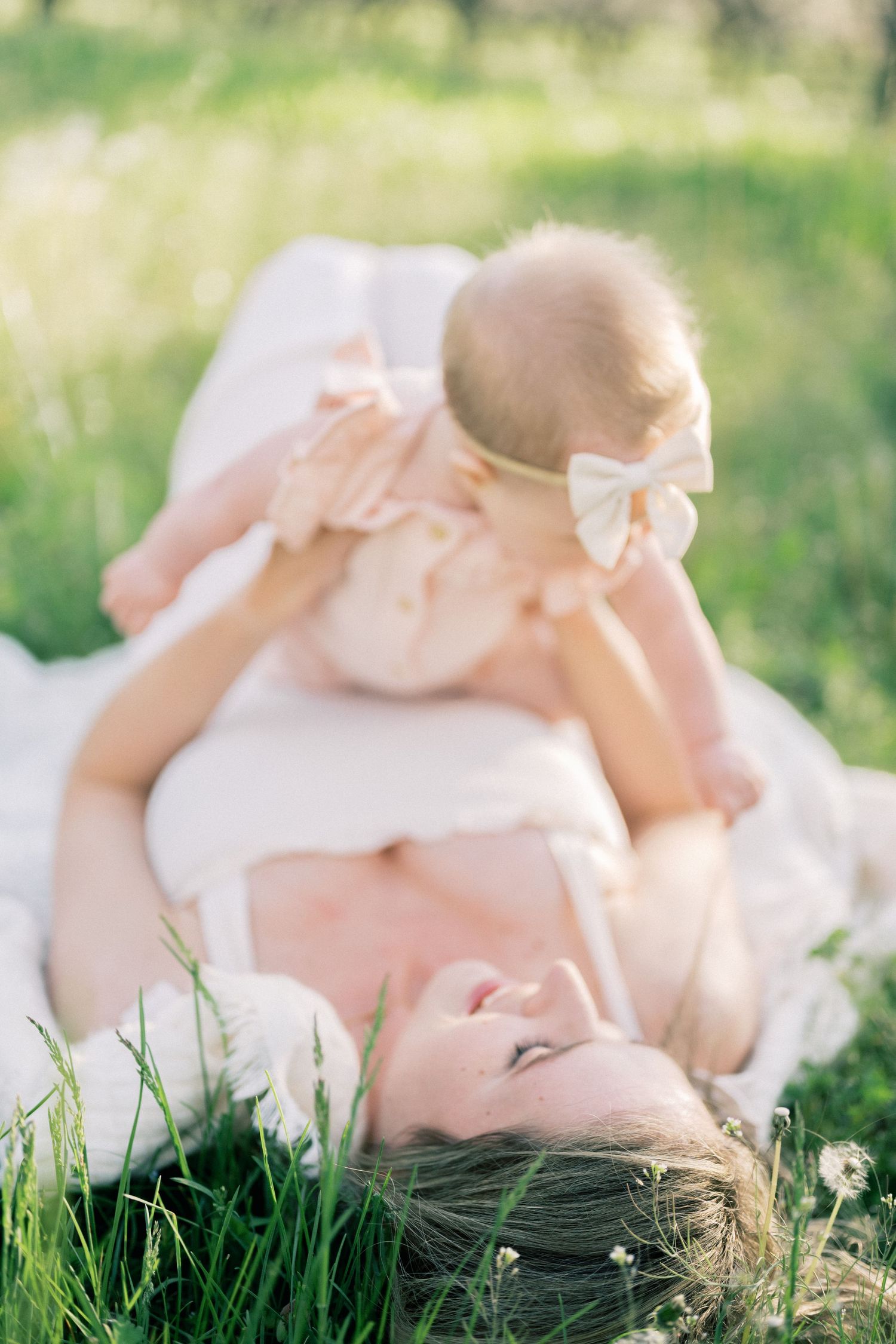 Sweet bonding moment captured outdoors with baby in peach dress lying on soft grass during golden hour.