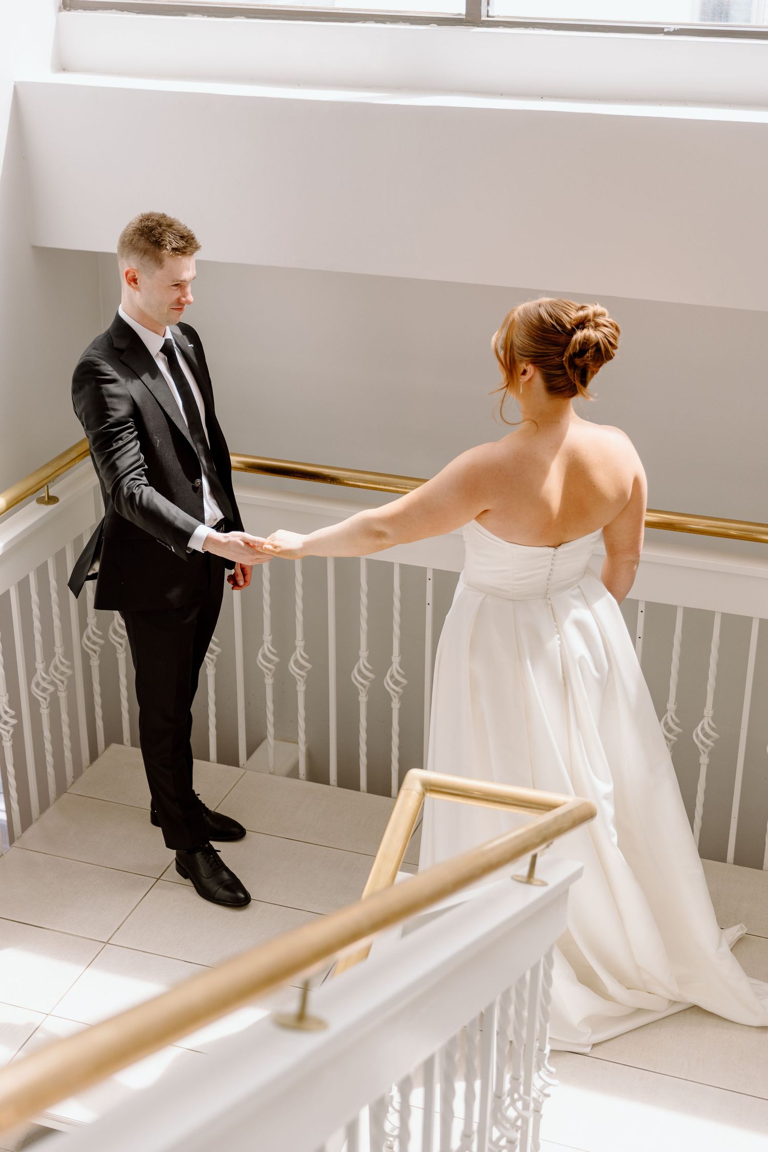 A couple shares a special first look moment on an elegant white staircase during their wedding.