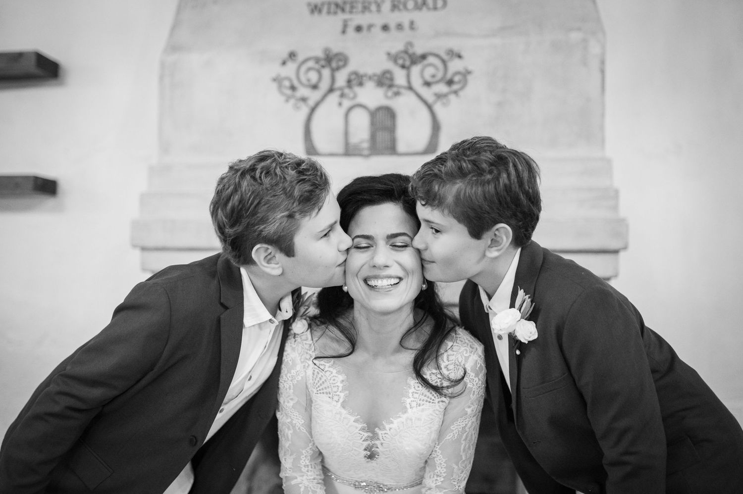 Black and white wedding photograph showing joyful moment between three people in formal attire.