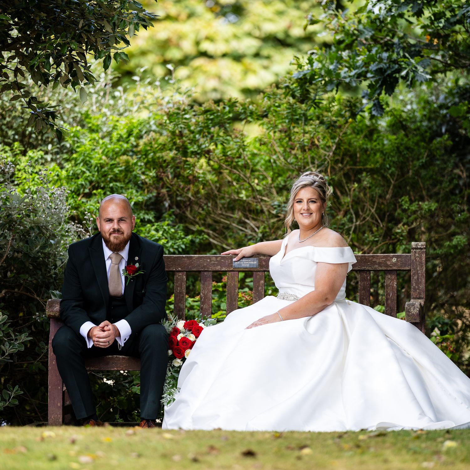 Wedding couple shares intimate moments in lush garden setting with wooden bench during outdoor photo session.