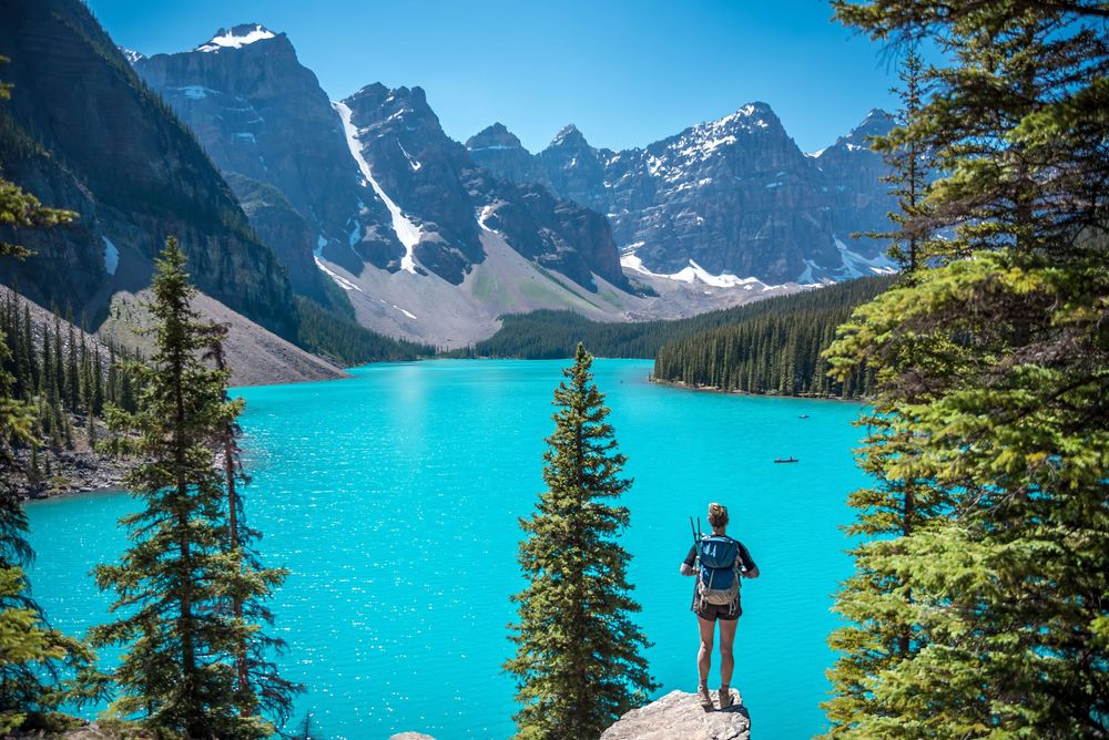 Hiker stands on viewpoint overlooking the stunning turquoise waters of Moraine Lake in Banff.