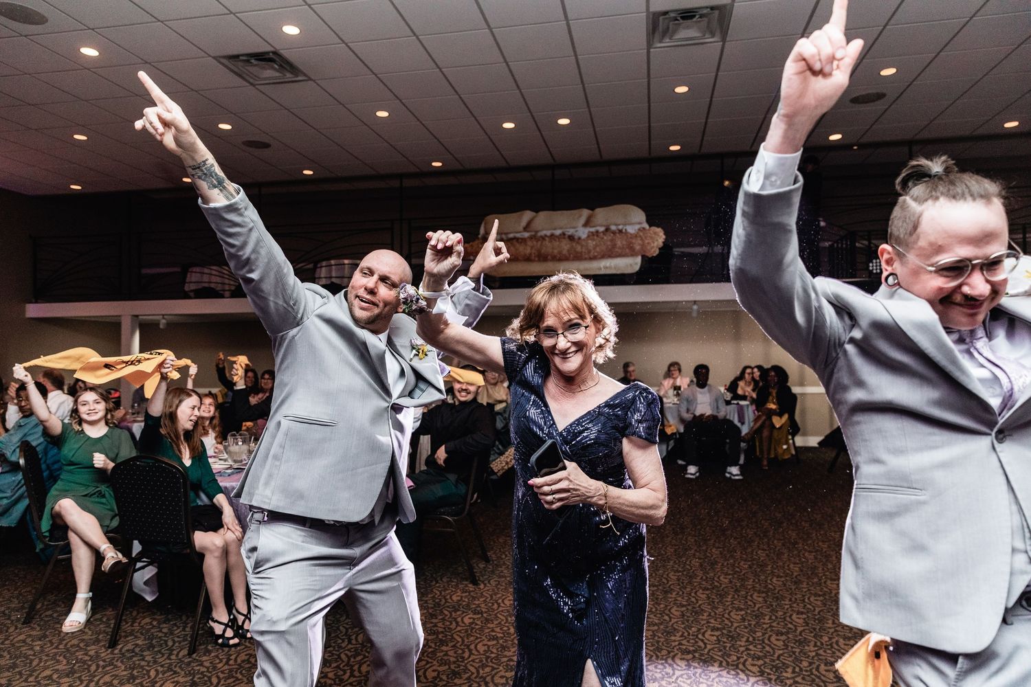 People dancing and celebrating enthusiastically at a wedding reception in a banquet hall.