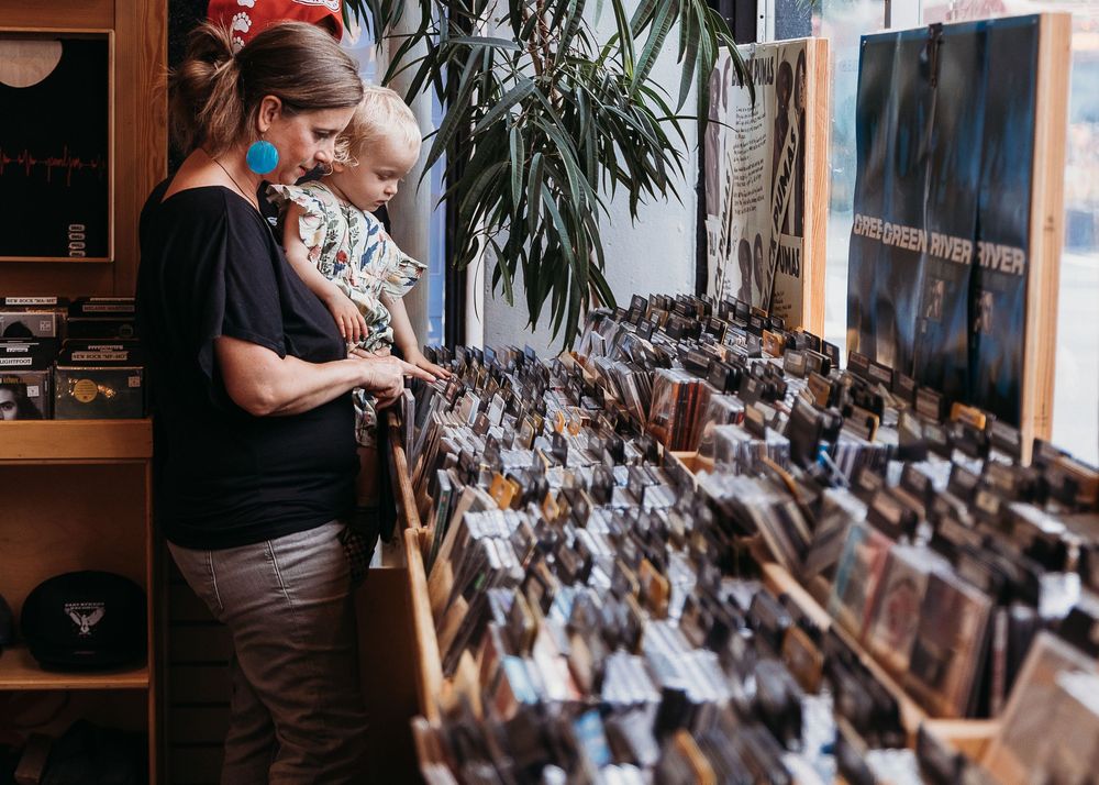 A person browses through organized vinyl records displayed on wooden shelves in a retail store.