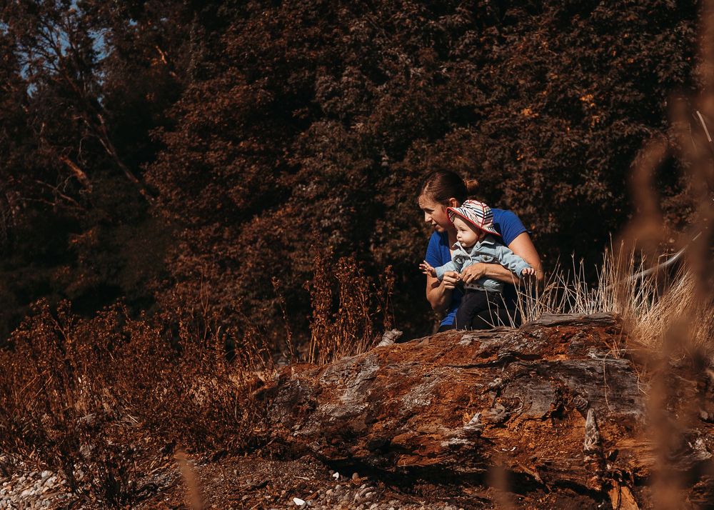 Two people sit together on a dirt slope overlooking autumn woods in warm afternoon sunlight.