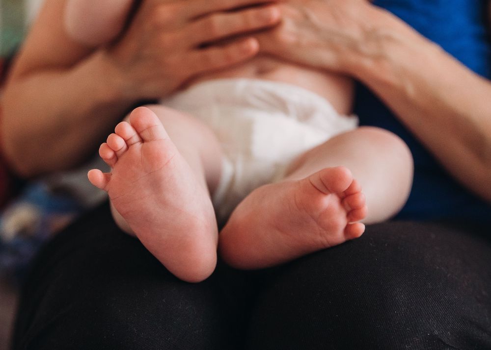 Close-up view of tiny baby feet resting on someone wearing dark clothing in soft natural light.