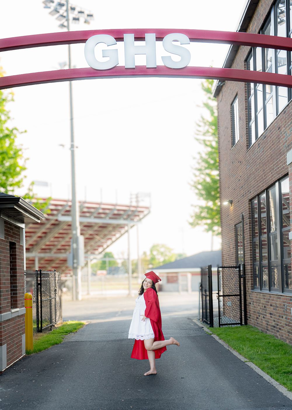 A view of a school entrance with a red GHS arch sign over a walkway and sports field lights visible in the background.