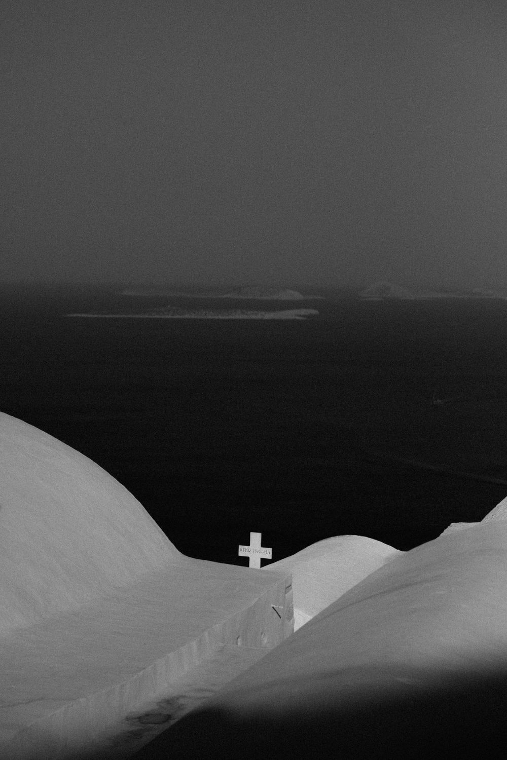 Minimalist black and white landscape with a small white cross against a dark horizon. Astypalaia wedding photographer Greece