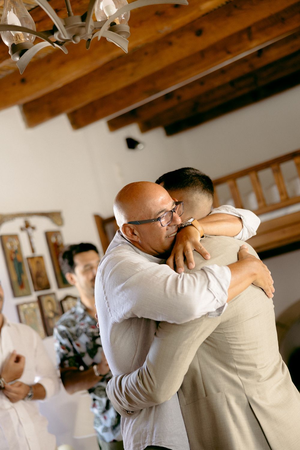 Two people sharing an emotional embrace in a room with exposed wooden beams. Astypalaia wedding photographer Greece
