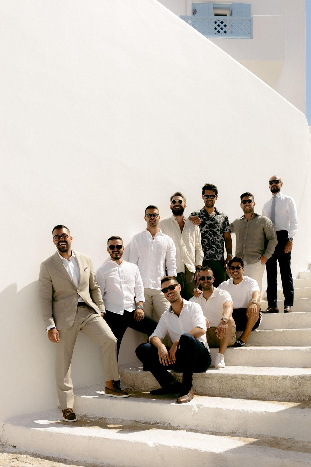 Groomsne in light colored clothing posing on white steps against Mediterranean architecture. Astypalaia wedding photographer Greece