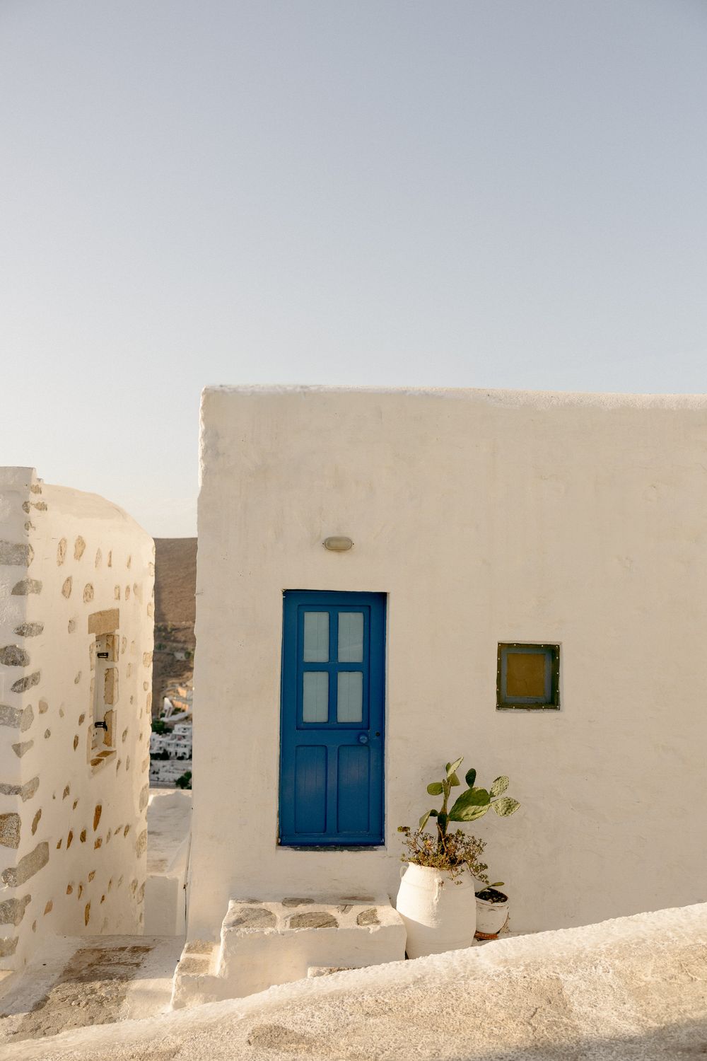 White Mediterranean building with bright blue door and small potted plant against clear sky. Astypalaia wedding photographer Greece