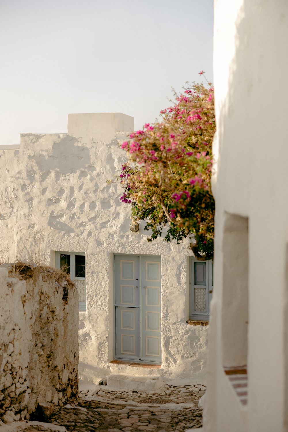 Pink bougainvillea flowers bloom against white walls and blue doors in Mediterranean alley. Astypalaia wedding photographer Greece