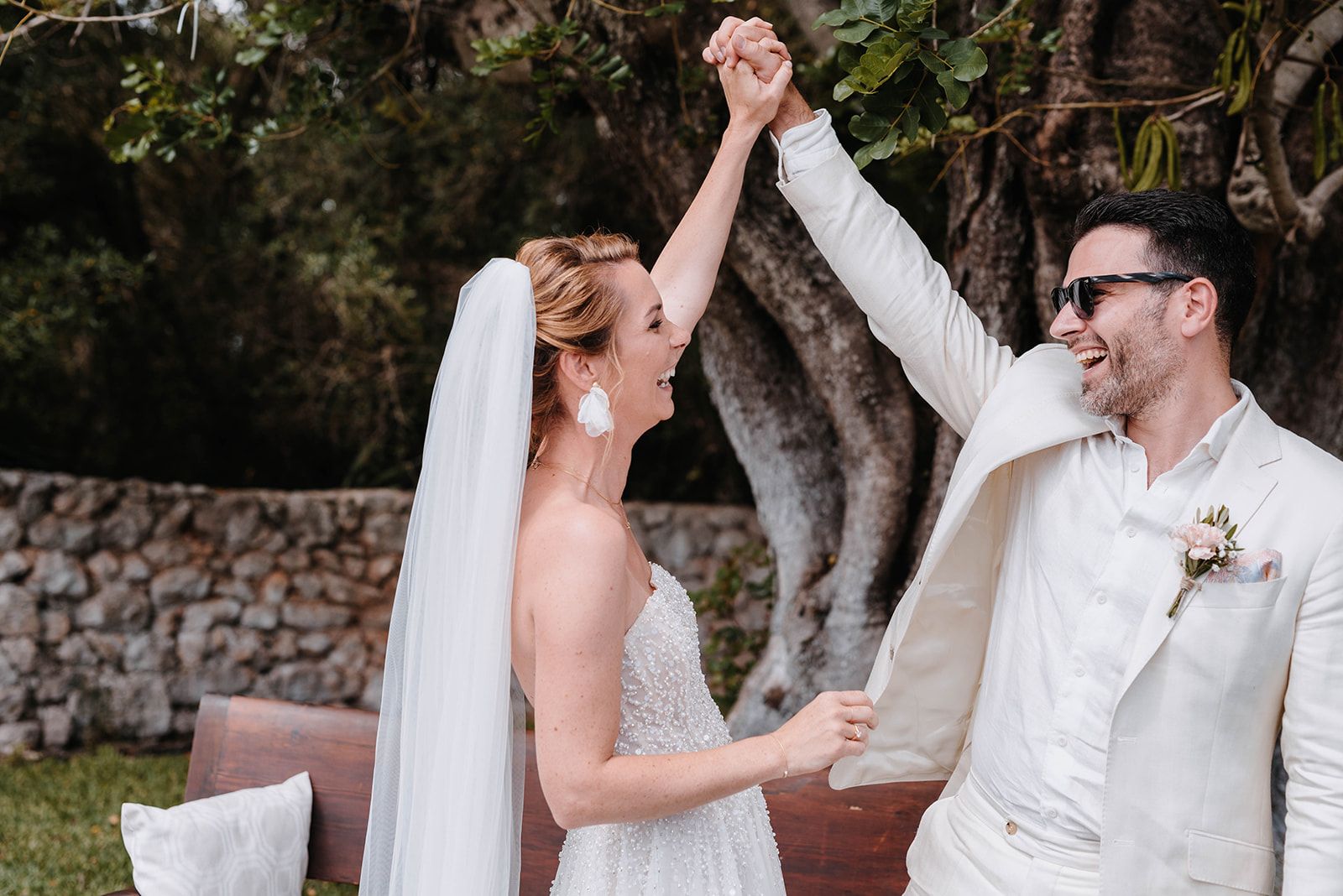 Joyful newlyweds celebrating with raised hands during outdoor wedding ceremony.