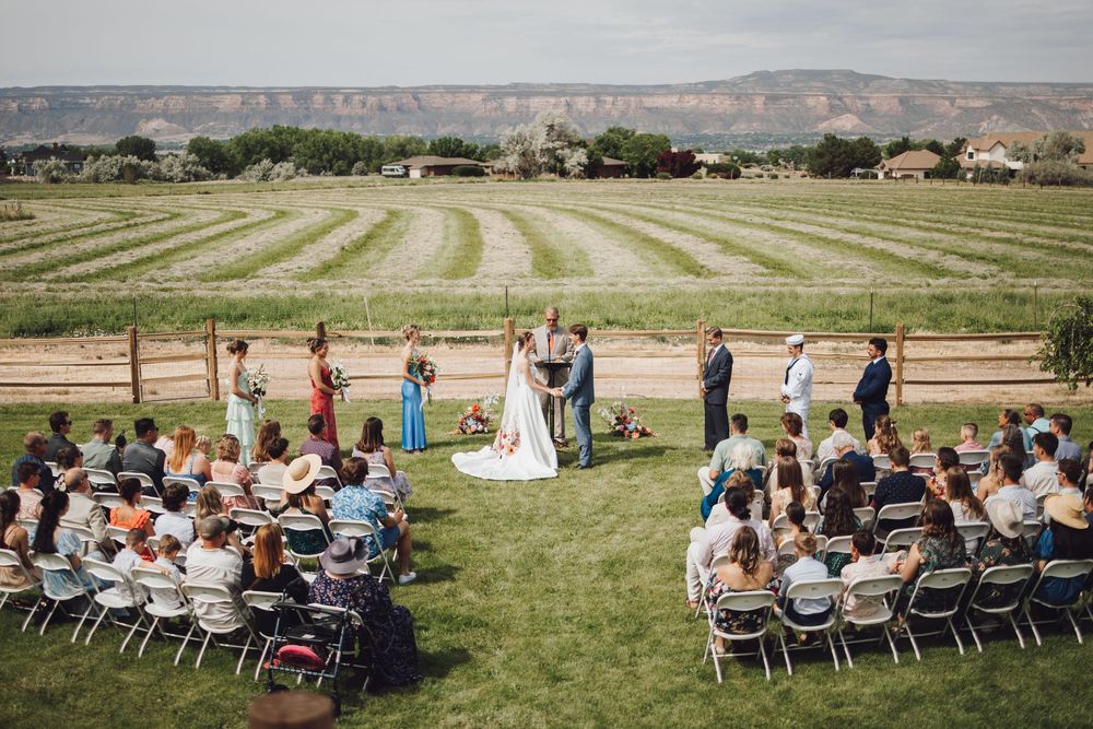 A Grand Junction Colorado wedding ceremony takes place on a manicured lawn overlooking striped agricultural fields and distant mountains.