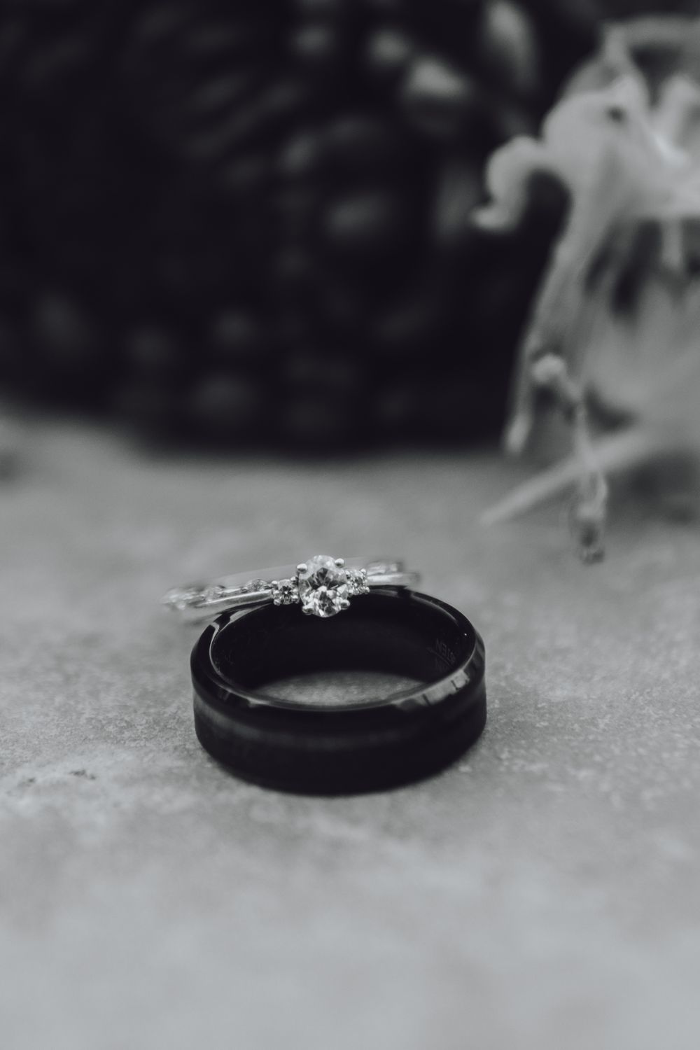 Black and silver wedding rings displayed in artistic black and white macro photography on concrete surface.