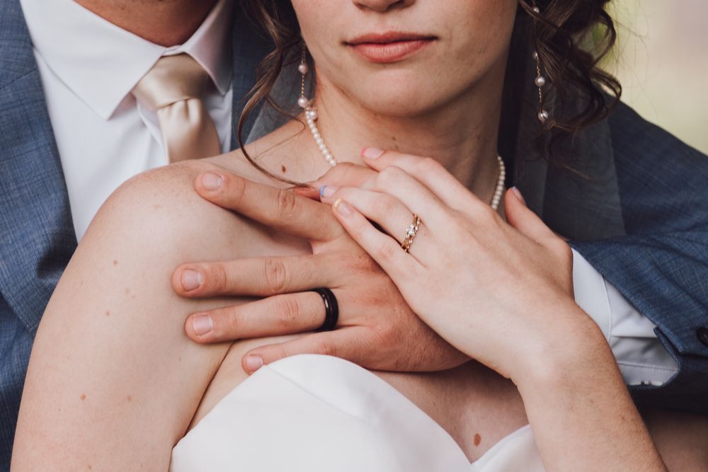 Closeup of hands showing wedding rings and tender embrace between couple in formal wedding attire. Grand Junction wedding photographer