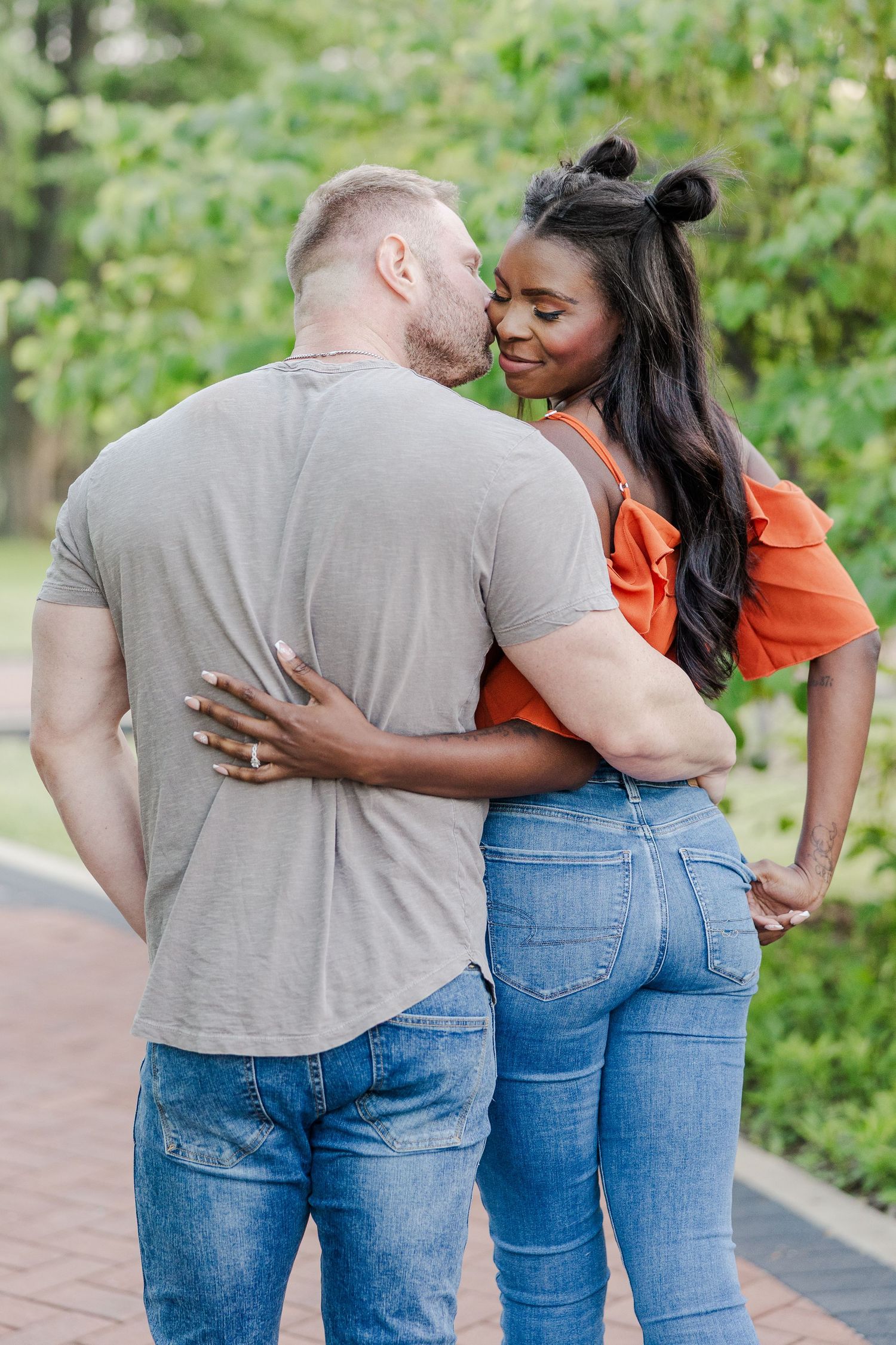 A couple sharing an intimate romantic moment while embracing on a brick path surrounded by lush greenery.