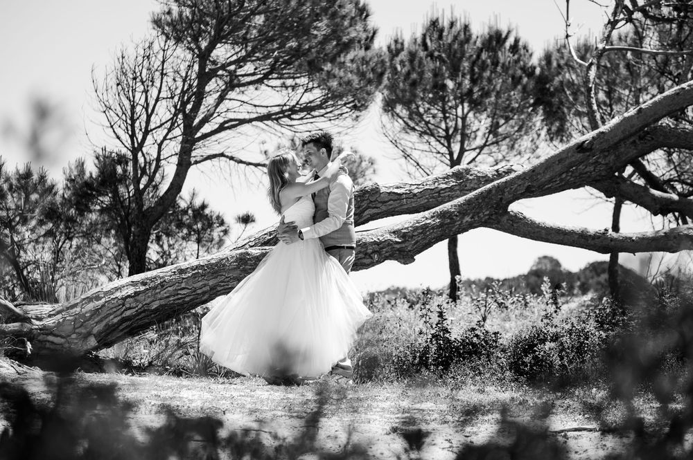 Artistic black and white portrait showing a graceful figure in a flowing white dress balanced on a fallen tree branch.